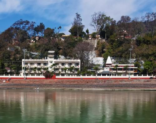 un grand bâtiment blanc à côté d'une étendue d'eau dans l'établissement Yog Niketan By Sanskriti, à Rishikesh