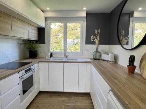 La cuisine est équipée de placards blancs, d'un lavabo et d'un miroir. dans l'établissement Appt Vue Mer Exceptionnelle Triple Expo - 70m 2ch - Rénové, à Saint-Cast-le-Guildo