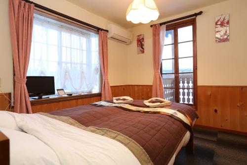 a bedroom with a bed and two windows and a television at Alpine Wind in Hakuba