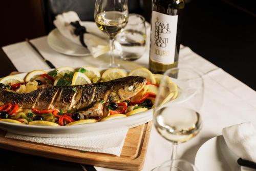 a plate of food with a fish on a table with wine glasses at Design & Wine Hotel in Caminha