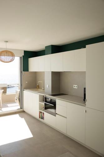 une cuisine avec des placards blancs et une grande fenêtre dans l'établissement Le pied dans l'eau, à Palavas-les-Flots