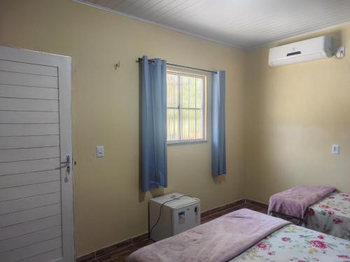 a bedroom with two beds and a window with blue curtains at Casa Azul in Barreirinhas