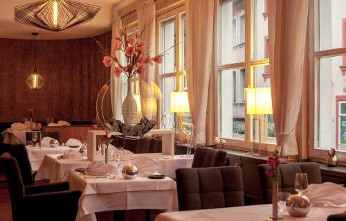 un restaurante con mesas y sillas blancas y ventanas en Hotel Saarburger Hof en Saarburg