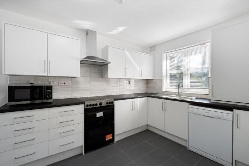a kitchen with white cabinets and a black appliance at Roomy 3 bedroom house, 2 baths in Edgware