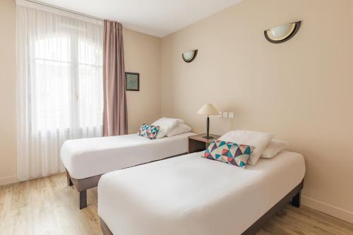 two beds in a room with a window at Appart'City Confort Agen Centre in Agen