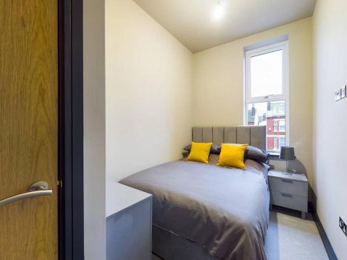 a bedroom with a bed with yellow pillows and a window at Gibson Manor Apartment 10 in Wallasey