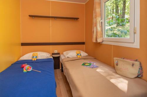 two twin beds in a room with a window at Camping maeva Escapades Le Domaine Aramis in Marsan
