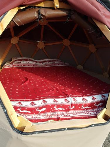 a bed with a red blanket in a suitcase at Camping écovillage Soleil du Pibeste in Agos-Vidalos