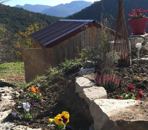 un jardin avec un petit hangar et des fleurs dans la saleté dans l'établissement Les Chemins de l'osier, à Vachères-en-Quint