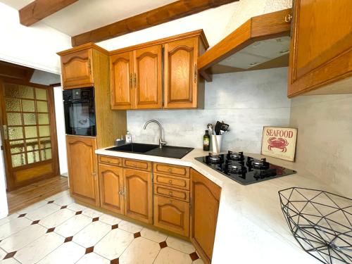 cocina con armarios de madera, fregadero y fogones en Maison chaleureuse proche mer en Piriac-sur-Mer