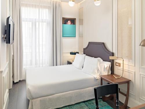 a bedroom with a bed and a table and a window at Boutique Hotel H10 Villa de la Reina in Madrid