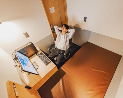 a person sitting in a room with a laptop at Relief Kokura ANNEX Book & Stay in Kitakyushu