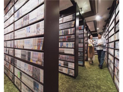 two people walking through a library aisle with books at Relief Kokura ANNEX Book & Stay in Kitakyushu