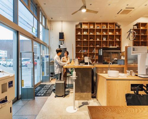 two people standing at a counter in an office at Relief Kokura ANNEX Book & Stay in Kitakyushu