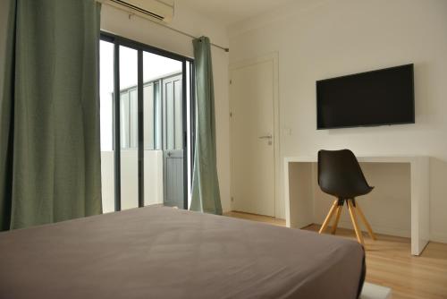 um quarto com uma cama, uma televisão e uma cadeira em Duarte Apartments - Lux em Mindelo
