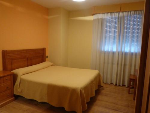 1 dormitorio con 1 cama y una ventana con cortinas en El Ancla, en Ponferrada