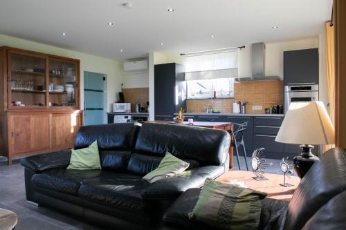 a living room with a black leather couch and a kitchen at Côté Jardin in Buvrinnes