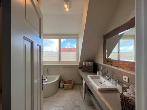 La salle de bains est pourvue d'un lavabo, d'une baignoire et d'un miroir. dans l'établissement Peeneblick - Traumhaus direkt am Wasser mit eigenem Bootssteg für 8 Personen, à Rankwitz
