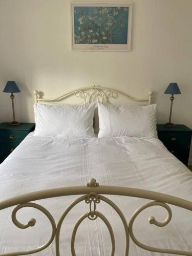 a bed with white sheets and pillows and two lamps at Centrally located flat with parking in Tetbury