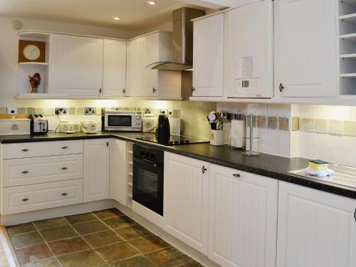 una cocina blanca con armarios y electrodomésticos blancos en Owl Cottage, en Coedana