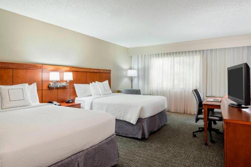 a hotel room with two beds and a flat screen tv at Courtyard by Marriott Gainesville FL in Gainesville