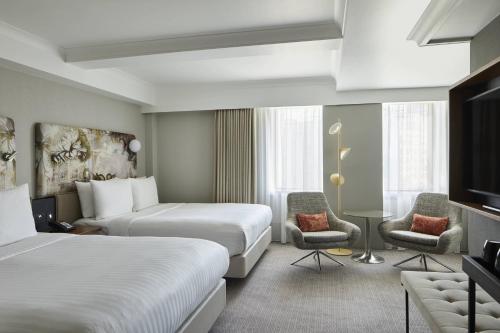 a hotel room with two beds and two chairs at London Marriott Hotel Kensington in London