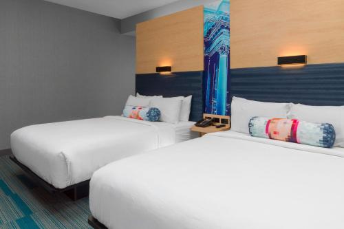 two beds in a hotel room with white sheets and pillows at Aloft Gainesville University Area in Gainesville