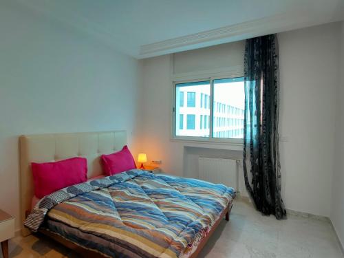 Schlafzimmer mit einem Bett mit rosa Kissen und einem Fenster in der Unterkunft FLAT JINEN DU LAC 2 in Tunis