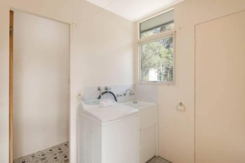 ein weißes Bad mit einem Waschbecken und einem Fenster in der Unterkunft Sea Home With a View at Pambula Beach-Pet Friendly in Pambula Beach