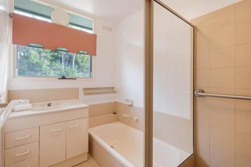 Un baño con bañera, lavabo y ducha. en Sea Home With a View at Pambula Beach-Pet Friendly, en Pambula Beach