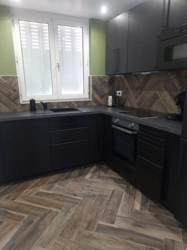 une cuisine avec des armoires noires et un plancher en bois dans l'établissement Charmant appartement proche de la défense, à Rueil-Malmaison