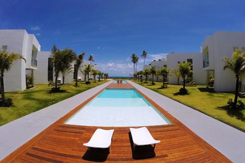 a swimming pool with two white chairs next to some buildings at B Blue Beachouses in Itacimirim