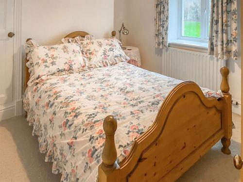 a bedroom with a wooden bed with a floral bedspread at New Cottage in Penmaenpool