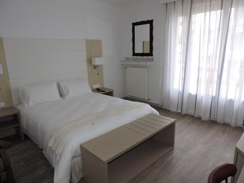 a white bedroom with a large bed and a mirror at Hotel Uhainak in Hendaye