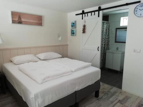 1 dormitorio con cama blanca y reloj en la pared en Strandhuisje DAAN dicht bij zee en strand, en Callantsoog