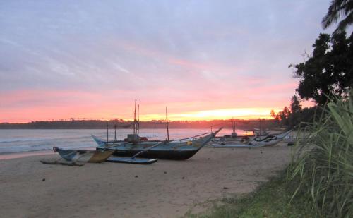 a group of boats sitting on the beach at sunset at Isana Beach House in Tangalle