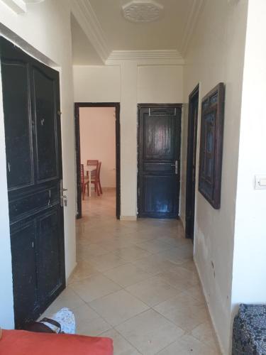 a hallway with black doors and a tile floor at Logement a 8mn de mehdia in Kenitra