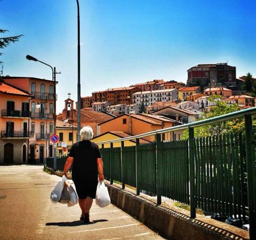 una mujer mayor caminando por una calle con bolsas de compras en La casa nel Borgo, en Bella