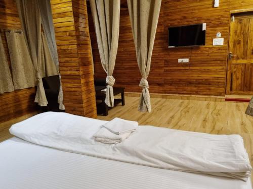 1 dormitorio con 1 cama con sábanas blancas y TV en Woods Residency en Jeypore