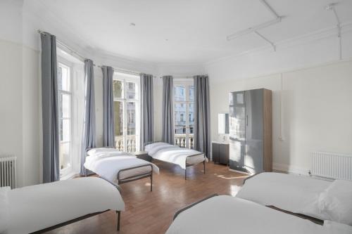 um quarto com 4 camas e janelas com lençóis brancos em Holland House (Victoria) em Londres