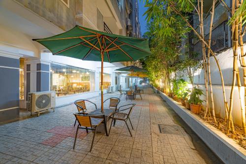 une table et des chaises avec un parasol vert sur le trottoir dans l'établissement Hotel Athome , Whitefields, Kondapur, à Hyderabad