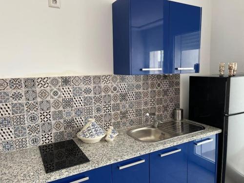 a kitchen with blue cabinets and a sink and a refrigerator at Studio Bleu Cosy à Dar Lili Djerba in Mezraya