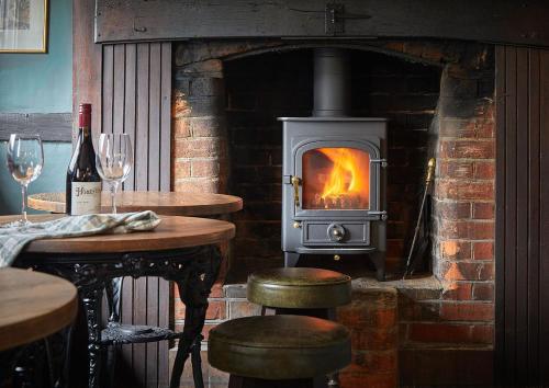 a brick fireplace with a stove with stools in front of it at The New Inn Heckfield in Hook