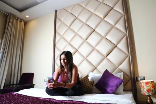 a woman sitting on a bed looking at her cell phone at Perfectstayz Premium Ganga Heights at Harkipauri Road in Haridwār