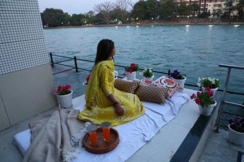 a woman in a yellow dress sitting on a table next to the water at Perfectstayz Premium Ganga Heights at Harkipauri Road in Haridwār