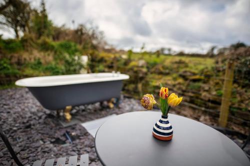 a vase of flowers sitting on a table next to a bath tub at Luxury Shepherd's Hut on Flower Farm with Outdoor Bath in Mid Cornwall in Truro