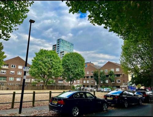 two cars parked in a parking lot with buildings in the background at Lovely 2BR Suite in Bow, E3 in London