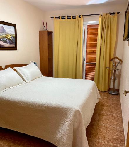 a bedroom with a white bed and yellow curtains at Los Alamos Somhome in Peniscola