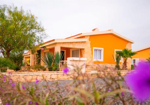 an orange house with flowers in front of it at Villa Atum. Stella Maris Exclusive in Vila do Maio