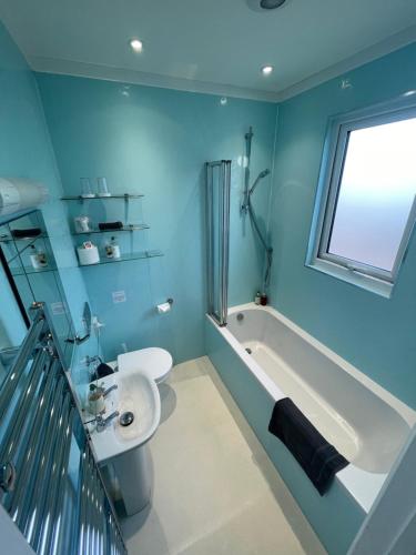 La salle de bains est pourvue de murs bleus, d'un lavabo et d'une baignoire. dans l'établissement Rivendell Room Only Studios, à Swanage